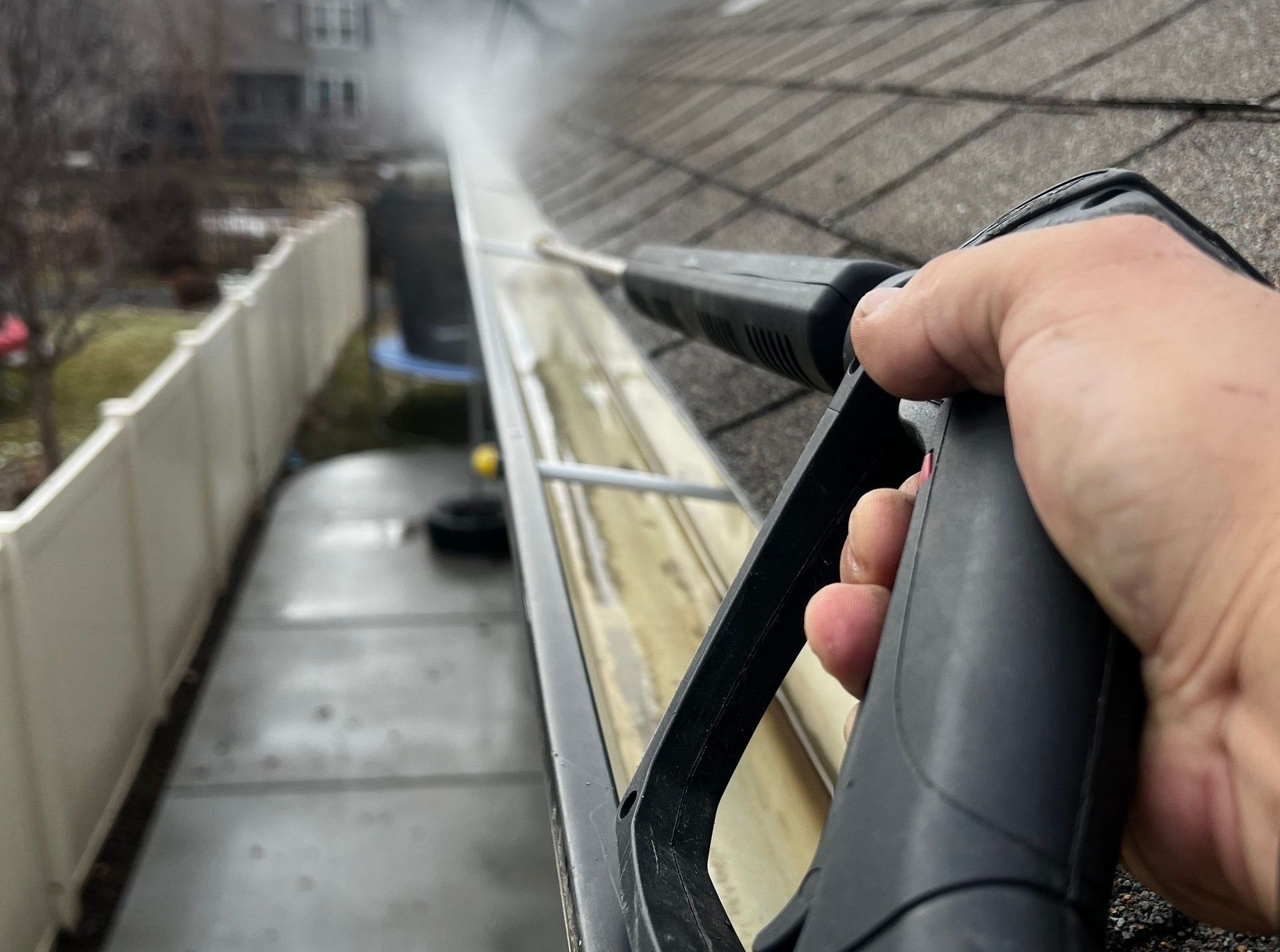 Close-up of gutter cleaning with pressure washer, outdoors, during the day.